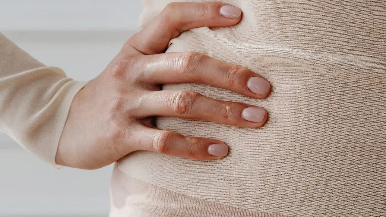 Mulher com a mão apoiada sobre o abdômen, em tons neutros