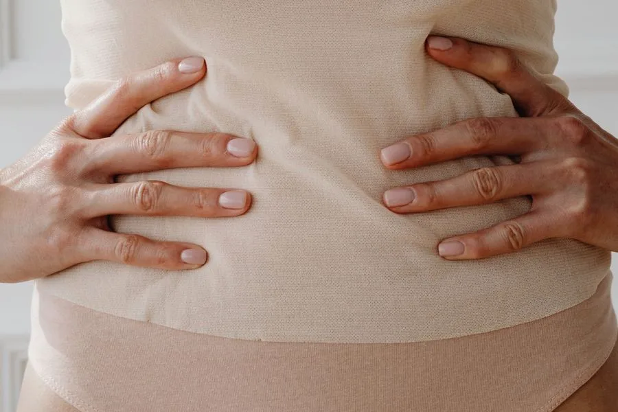 Mulher com as duas mãos apoiadas sobre o abdômen