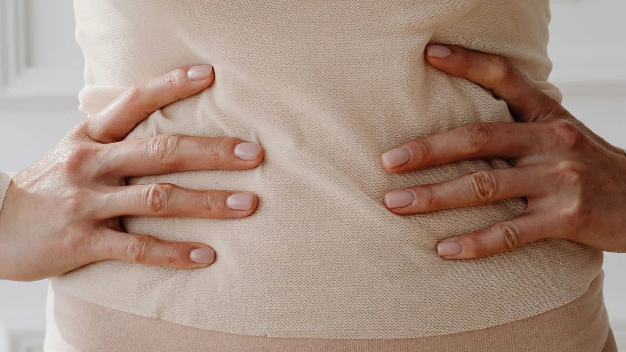 Mulher com as duas mãos apoiadas sobre o abdômen, em tons neutros